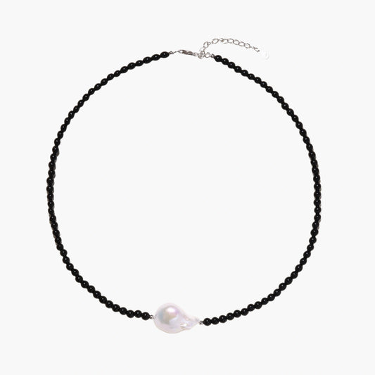 Beaded black agate necklace with iridescent baroque freshwater pearl centerpiece on cream background.
