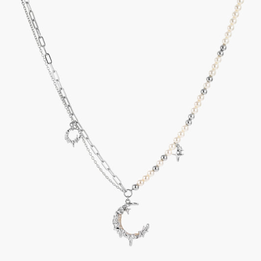 Silver-toned crescent moon pendant with star accents on pearl and chain necklace against white background.