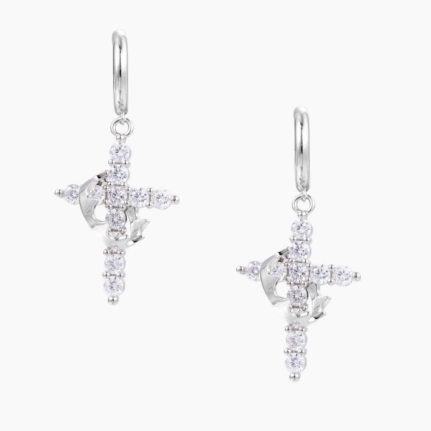 White gold-plated hoop earrings with sparkling zirconia cross charms dangling against cream background