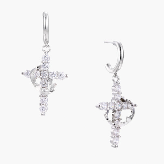 White gold-plated hoop earrings with sparkling zirconia cross charms dangling against cream background