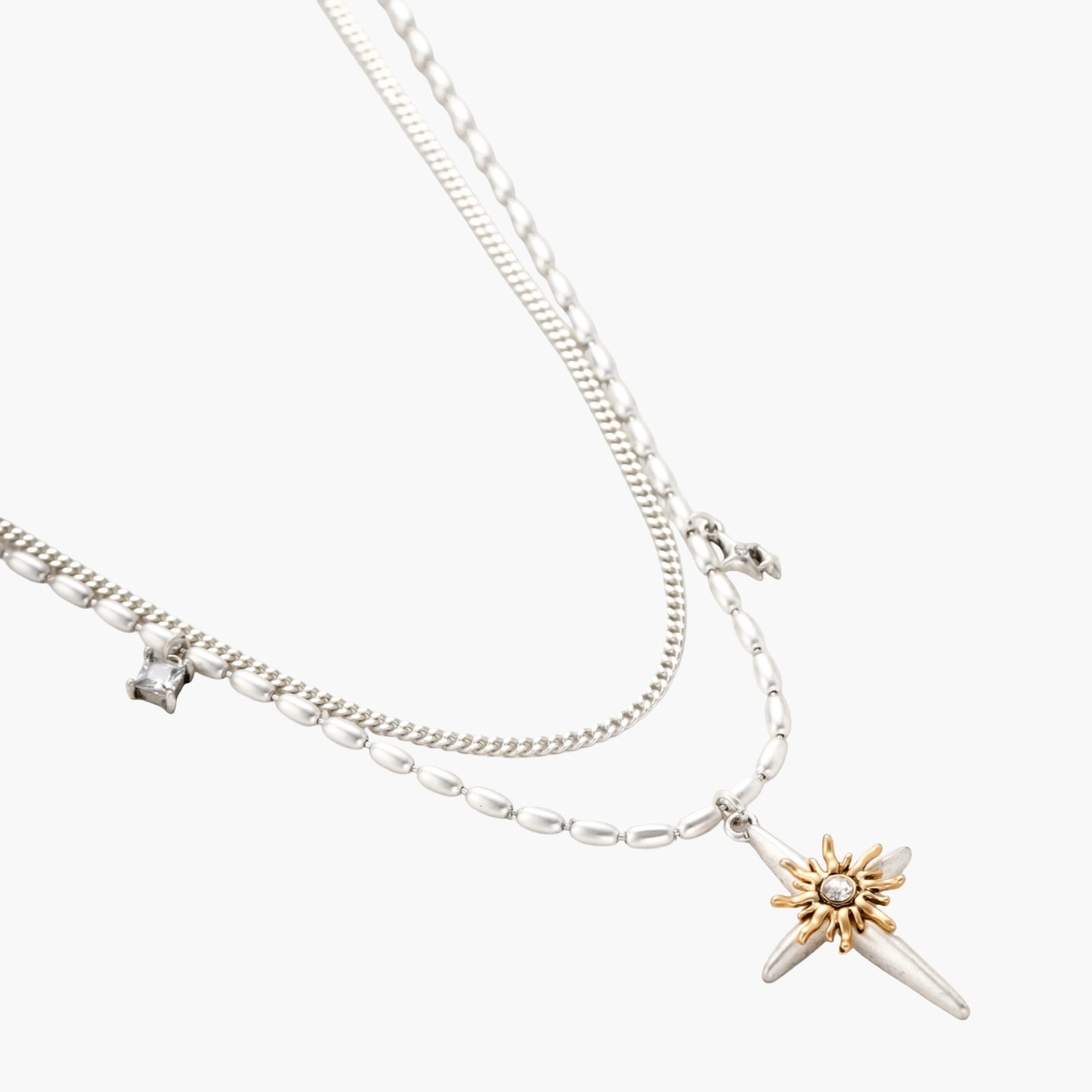 Layered silver-toned necklace set with cross pendant and gold sun charm detail, matching drop earrings on white background.