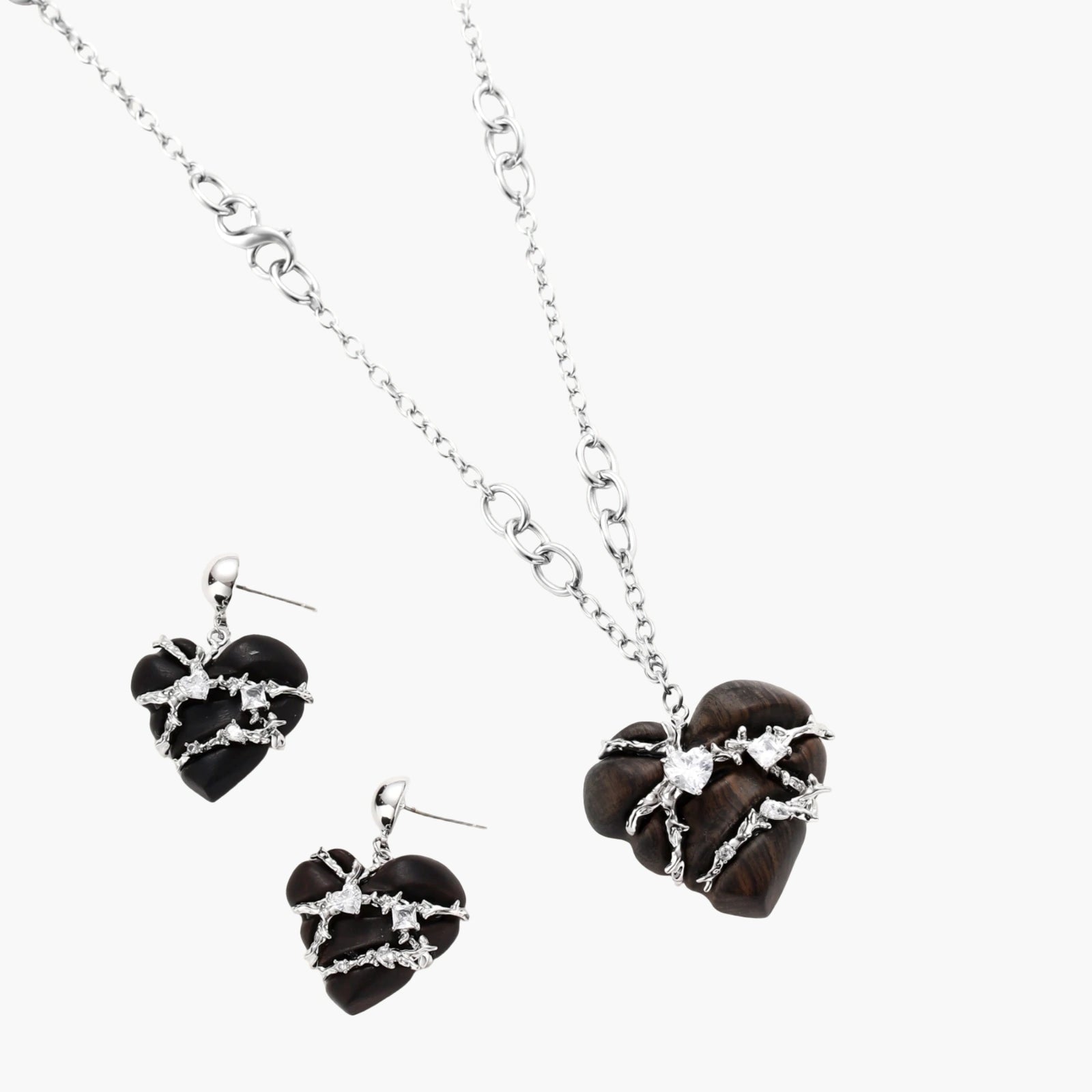 Dark ebony wood heart charms wrapped in intricate silver chains with crystal accents, shown as matching earrings and necklace set.