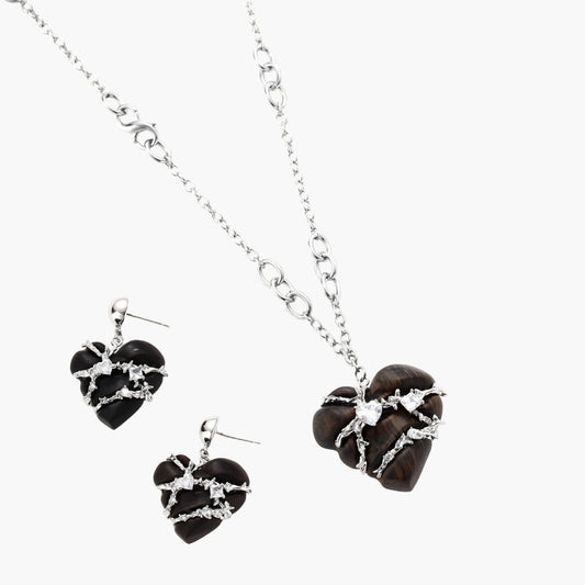 Dark ebony wood heart charms wrapped in intricate silver chains with crystal accents, shown as matching earrings and necklace set.
