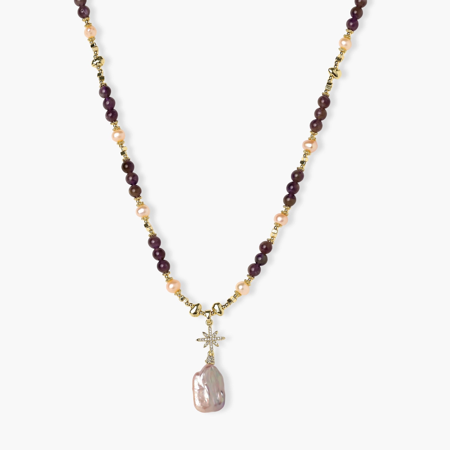 Gold necklace with iridescent baroque pearl pendant, purple amethyst beads, and crystal star charm on cream background